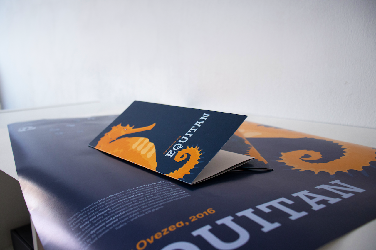 Ein dunkelblauer Folder mit Orangem Seepferdchen-Motiv liegt auf einem gleichfarbigen Plakat. Auf beiden steht Equitan groß in hellblauer Schrift. 